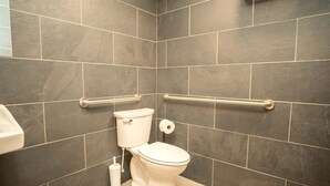 Un baño con baldosas oscuras, inodoro blanco, bidé y barras de apoyo.