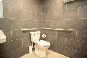 A bathroom with dark tiles, a white toilet, a bidet, and grab bars.