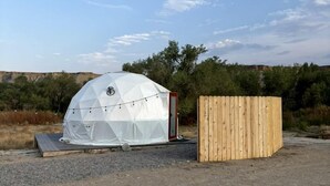 Una tienda en forma de cúpula geodésica con una estructura de madera a su lado.