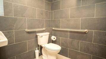 A bathroom with dark tiles, a white toilet, a bidet, and grab bars.