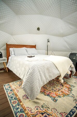 A bedroom with a bed, a bedside table, a lamp, and a patterned rug.
