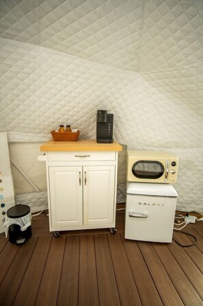 Una kitchenette con microondas, un refrigerador pequeño y un mueble con una cesta de objetos.