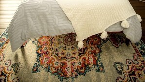 Un dormitorio con cama, mesita de noche, lámpara y alfombra estampada.