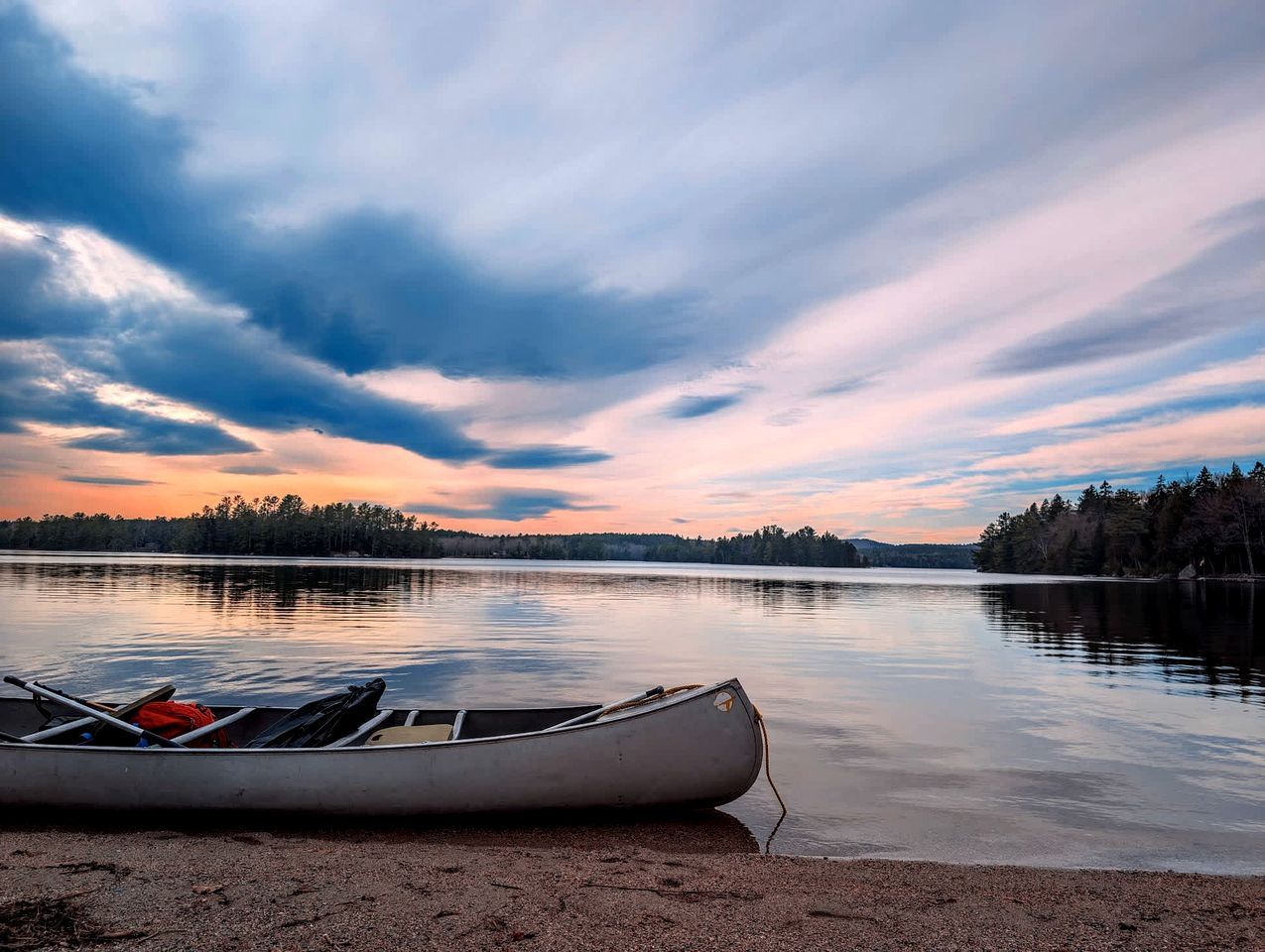 En kanot på en stilla sjö med en skogbeklädd strand.