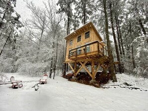 Una cabana de fusta amb un balcó, envoltada per un bosc nevós.
