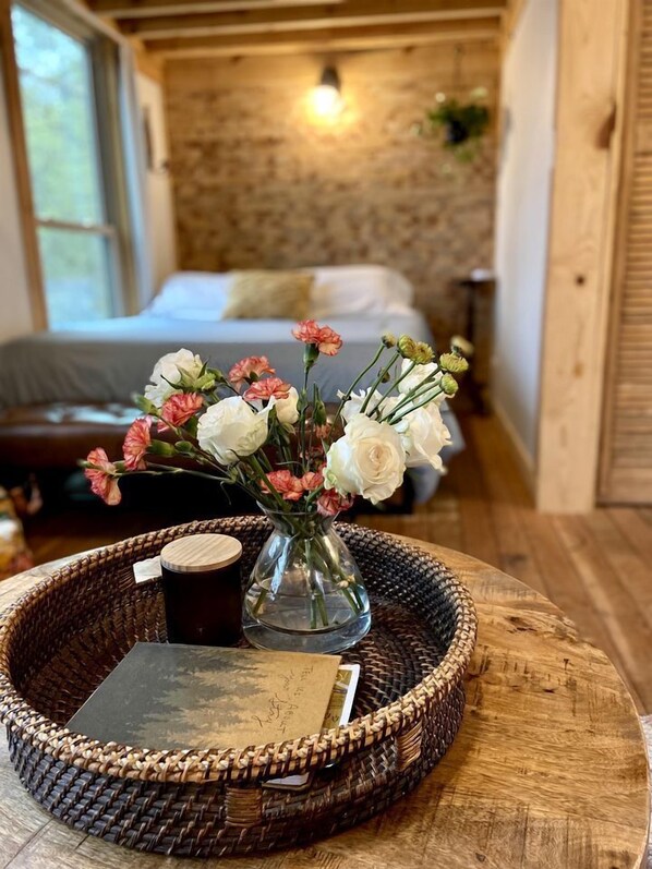 Una habitación con una cama, un jarrón con flores, una bandeja con un libro y una taza, y una pared de madera.
