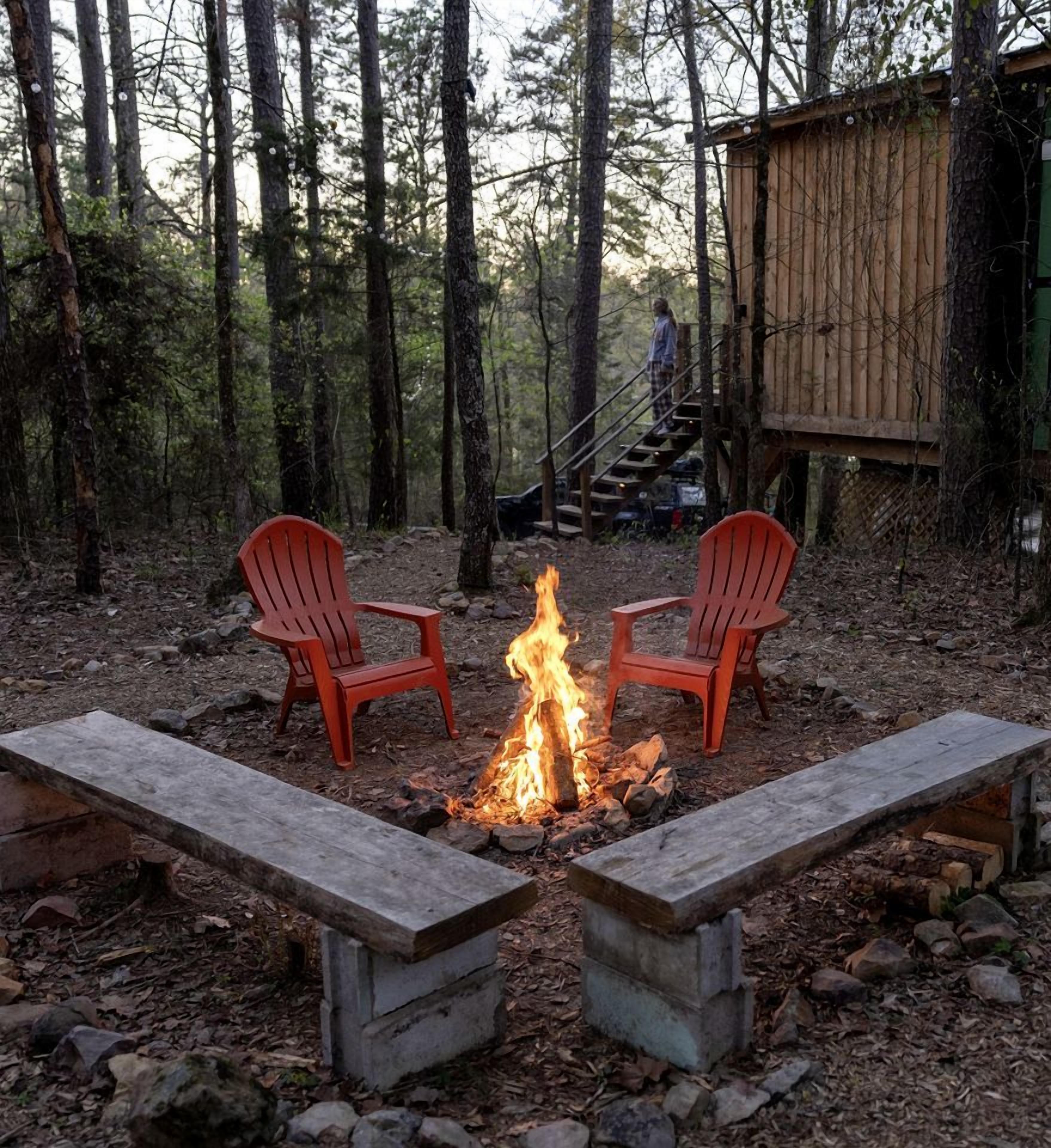 Lejrild med to røde Adirondack-stole, der vender mod det, omgivet af en skov.
