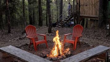 Lejrild med to røde Adirondack-stole, der vender mod det, omgivet af en skov.