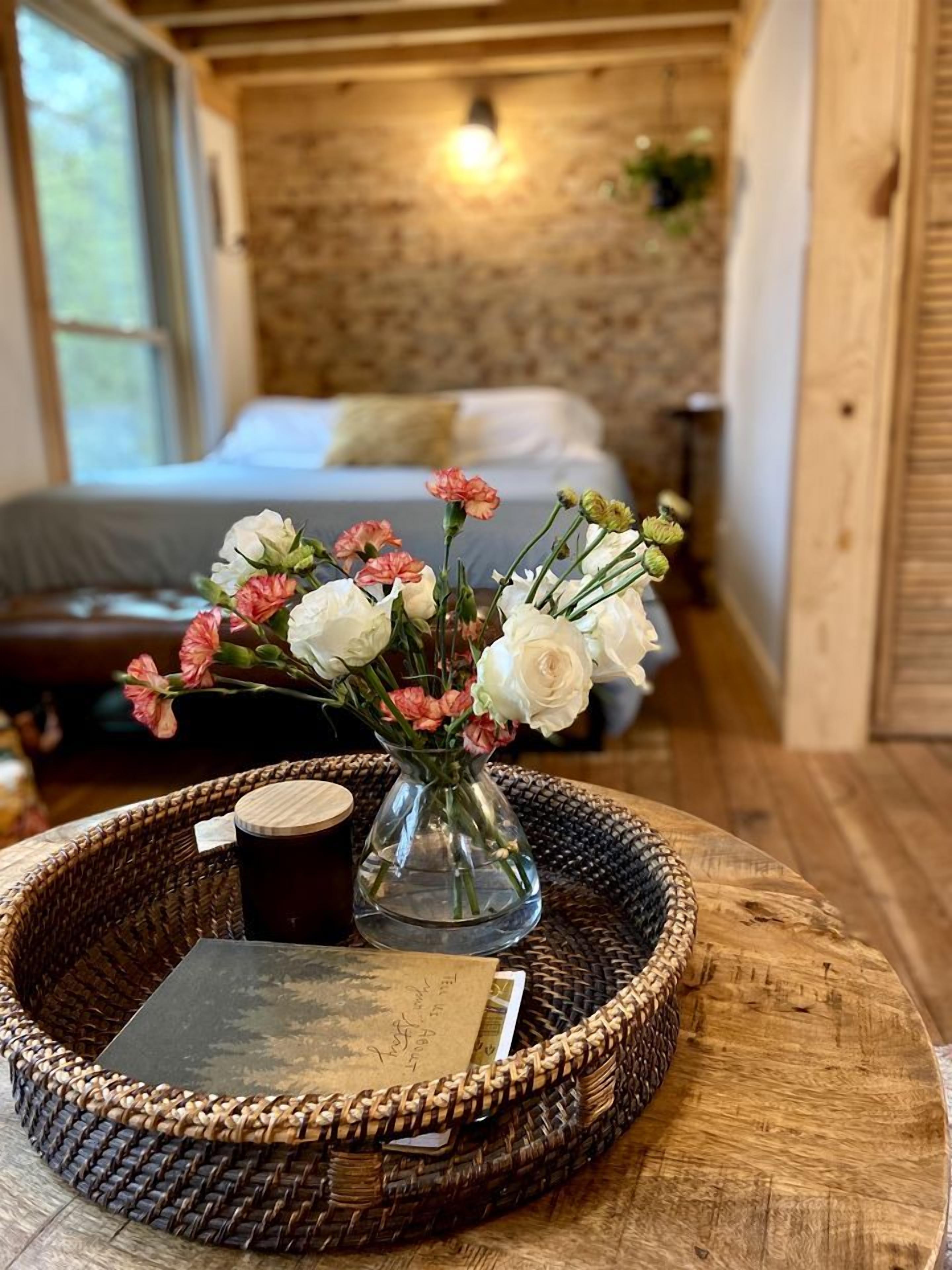 A room with a bed, a vase with flowers, a tray with a book and a mug, and a wooden wall.