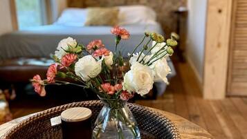 A room with a bed, a vase with flowers, a tray with a book and a mug, and a wooden wall.