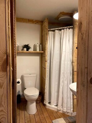 A wooden bathroom with a toilet, a shelf with toiletries, and a shower curtain. - Luminous Peaceful Treehouse with Incredible Forest Views and Fire Pit in Arkansas (Boles)