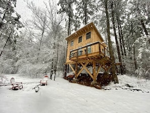 Una cabaña de madera con balcón, rodeada por un bosque nevado.