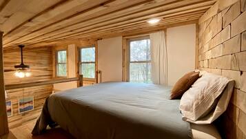 Quarto com teto de madeira, uma cama com travesseiro e uma janela.