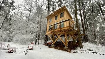 A wooden cabin with a balcony, surrounded by a snowy forest.