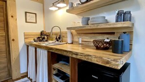 A compact kitchen with a wooden countertop, a sink, a dishwasher, and shelves above holding dishes and jars.
