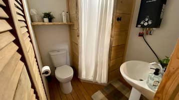 A compact bathroom with a toilet, shower curtain, sink, and a portable heater.