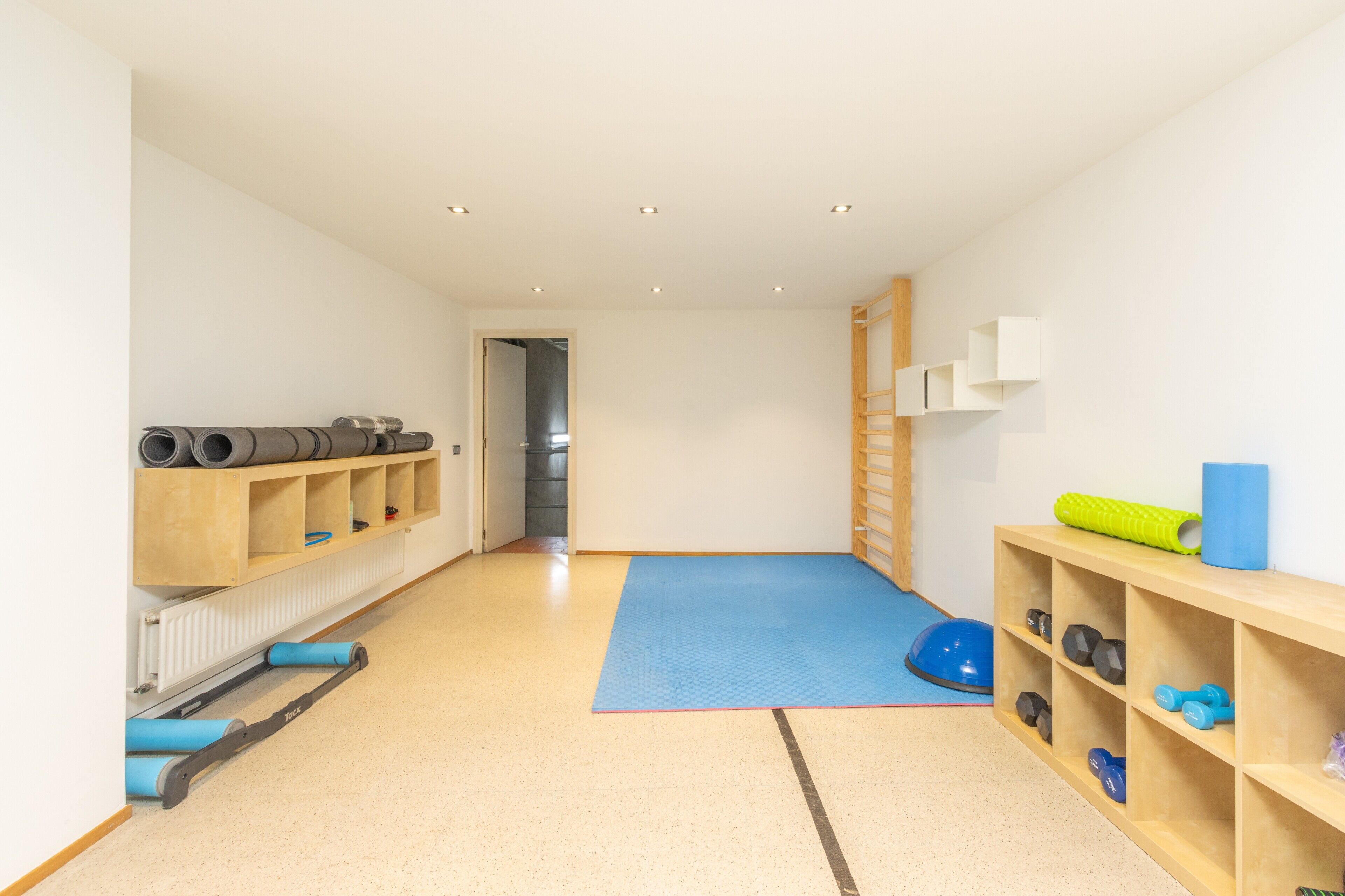 A room with a blue mat, shelves with exercise equipment, and a radiator.