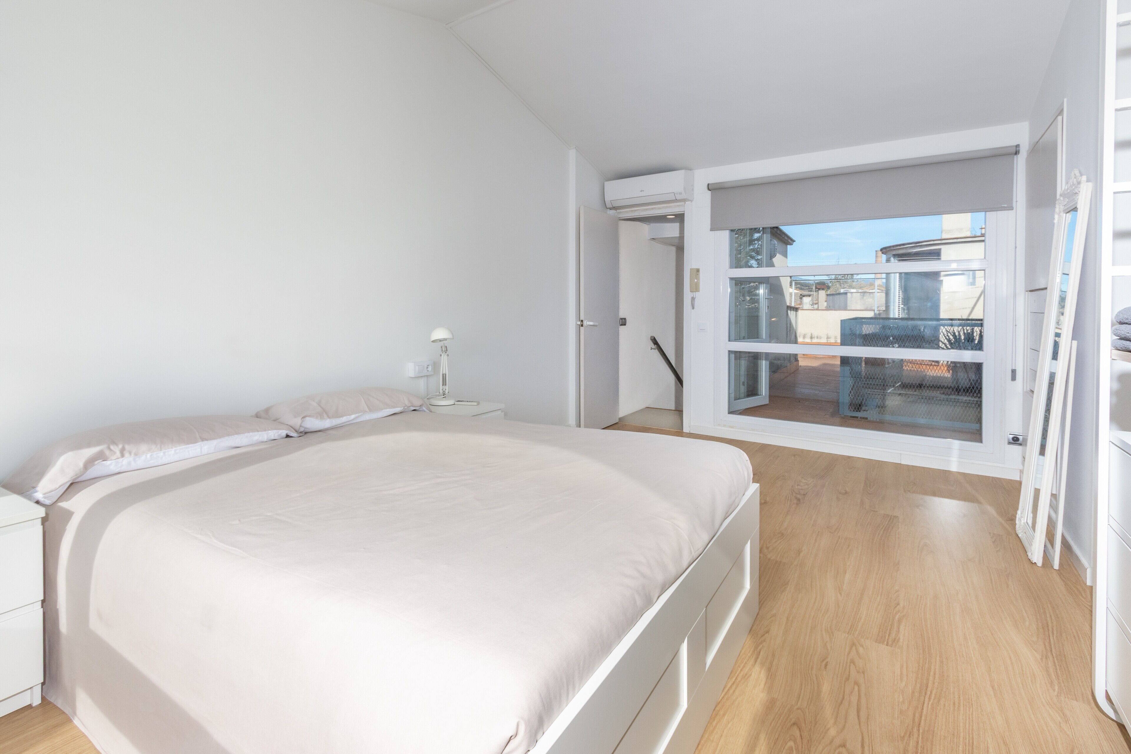 Una camera da letto con un letto grande, un comodino, una lampada e una porta scorrevole in vetro che dà su un balcone.
