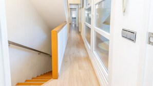 Un couloir étroit avec un escalier en bois, un radiateur et un téléphone fixé au mur.