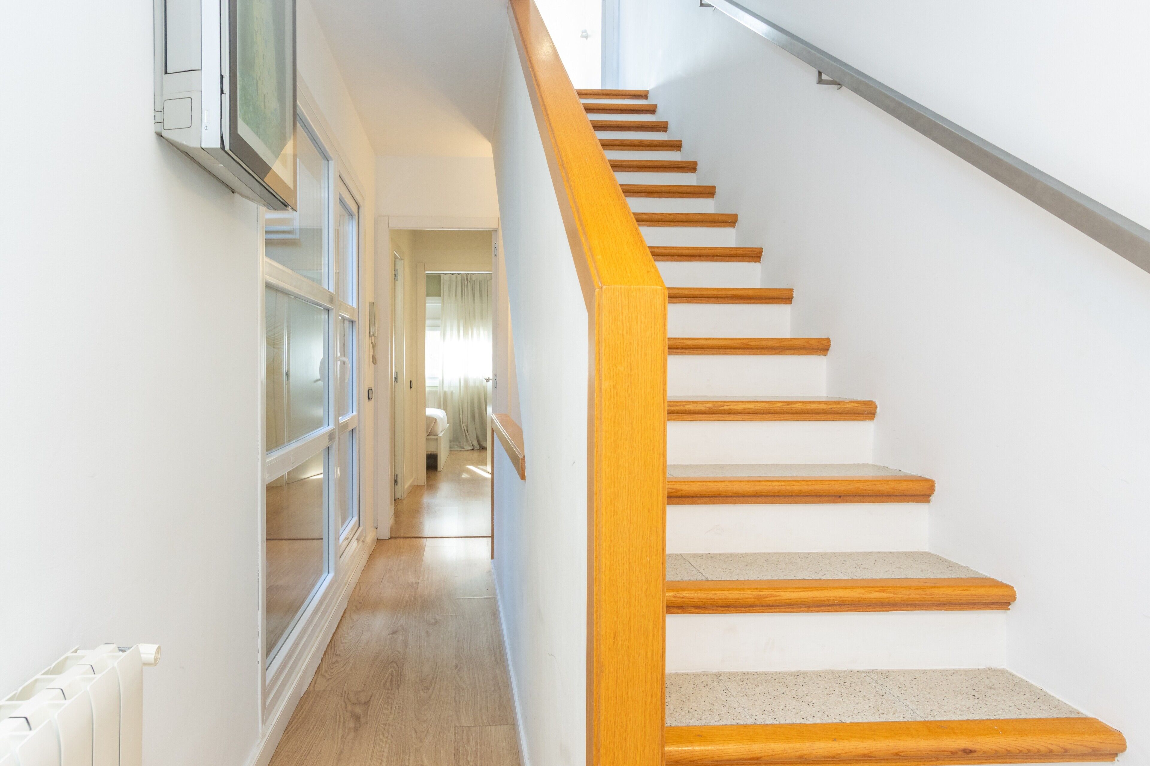 Una escalera de madera con barandilla que lleva a una habitación con radiador y ventana.