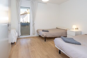 A bedroom with two beds, a small bedside table with a lamp, a sliding glass door to a balcony, and a white door. - Holiday Home 'Siker' with Private Terrace and Wi-Fi (Banyoles)
