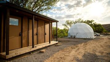 A wooden cabin with a covered porch and a dome tent in a desert setting.