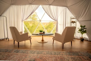 Una habitación con toldo, dos sillas, una mesita y vista a zonas verdes.