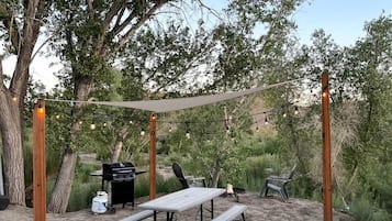 An outdoor patio with a table and chairs, a grill, and string lights.