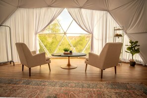 A tented room with two chairs, a small table, and a view of greenery.
