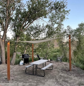 An outdoor patio with a table and chairs, a grill, and string lights.