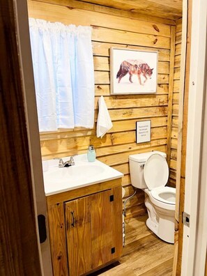 Un baño con paneles de madera, un lavamanos, un inodoro y un cuadro de un oso en la pared.