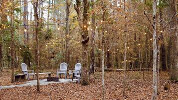 An outdoor seating area with chairs and a table, surrounded by trees and covered in fallen leaves.