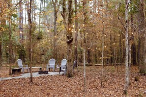 Un espace extérieur aménagé avec des chaises et une table, entouré d’arbres et recouvert de feuilles mortes.