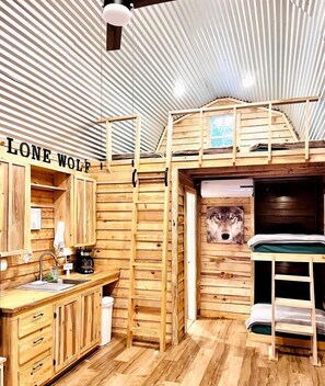 Interior de una cabaña con literas, paredes de madera, un lavabo y una ventana.