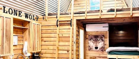 A cabin interior with a bunk bed, wooden walls, a sink, and a window.