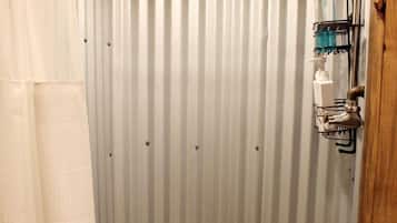 A shower with a wooden ceiling, a corrugated metal wall, and a handheld showerhead.