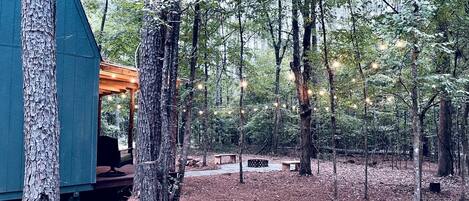 A forested area with a cabin, benches, and a covered seating area.