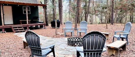 A rustic outdoor seating area with Adirondack chairs, a stone fire pit, and a small wooden table.