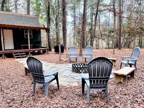 A rustic outdoor seating area with Adirondack chairs, a stone fire pit, and a small wooden table.