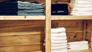 Una estantería de madera con toallas dobladas ordenadamente y una caja negra con el texto 'Make Makeup'.