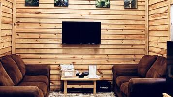 A cozy room with wooden walls, a ceiling fan, a flat-screen TV, two brown leather sofas, a small coffee table, and framed pictures on the wall.