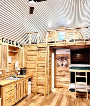 Interior de una cabaña con literas, paredes de madera, un lavabo y una ventana.