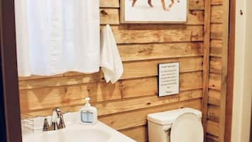 Une salle de bain rustique, aménagée dans une cabane en bois, avec un lavabo, des toilettes et un tableau représentant un loup accroché au mur.