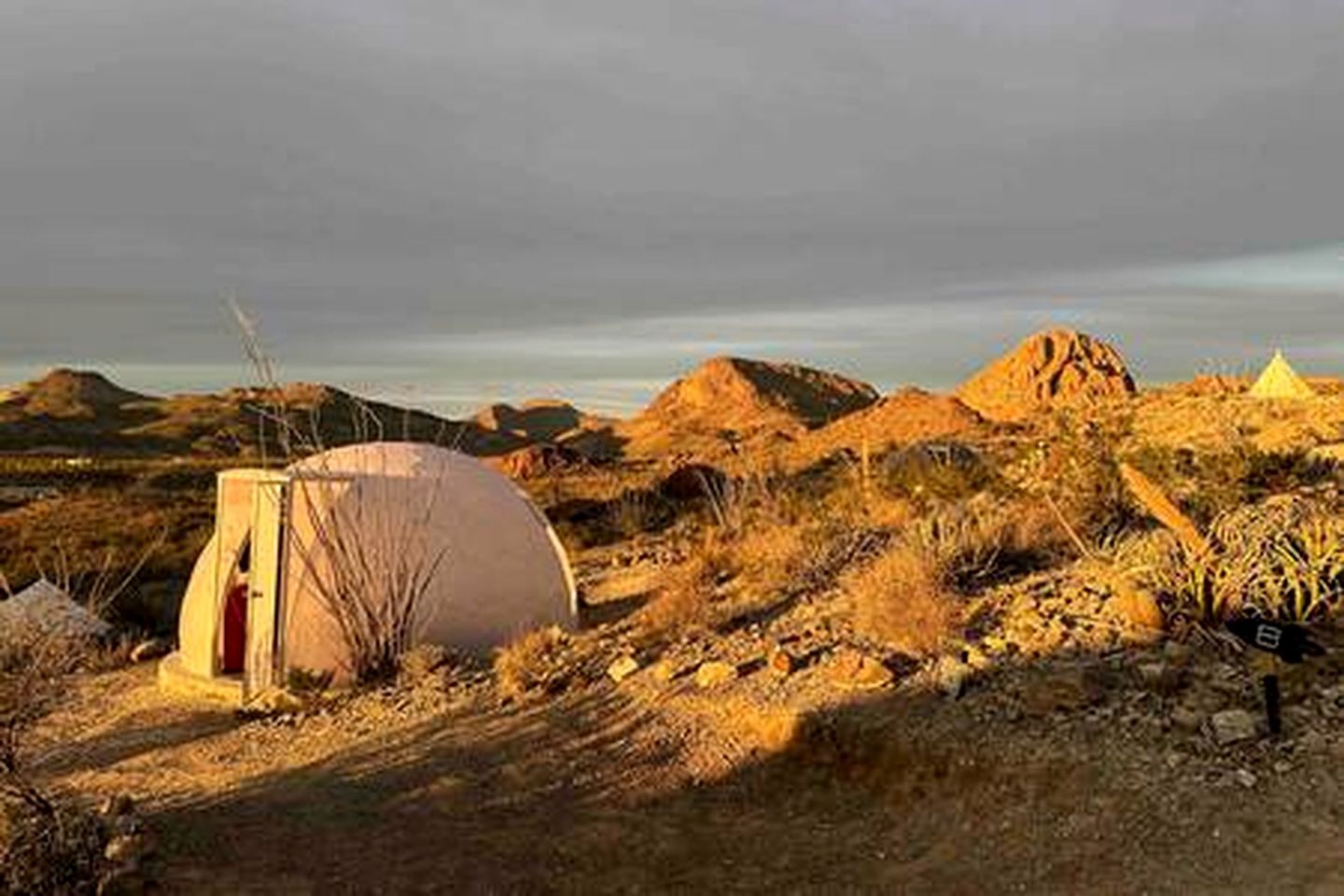 Een tent in een woestijnlandschap met rotsachtig terrein en schaarse begroeiing.