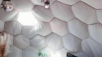 A room with a hexagonal patterned wall, a bed with pillows, and hanging lights.