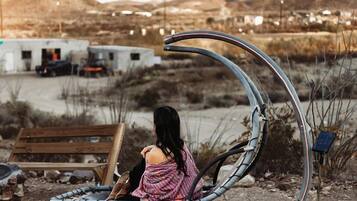 Una persona sentada en un banco metálico curvo en un paisaje desértico, con montañas al fondo.