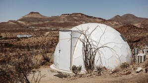 A dome-shaped structure in a desert landscape with mountains in the background.