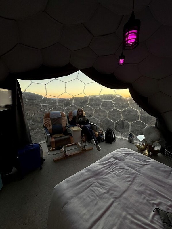 Una habitación con una cama grande, una silla y vistas a través de un ventanal hexagonal.