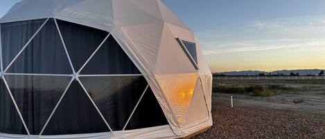 A geodesic dome structure with a black interior, set on a gravel surface with a clear sky in the background.