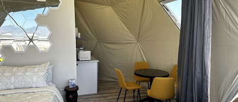A tented room with a bed, a small kitchenette, a dining table with chairs, and a window.